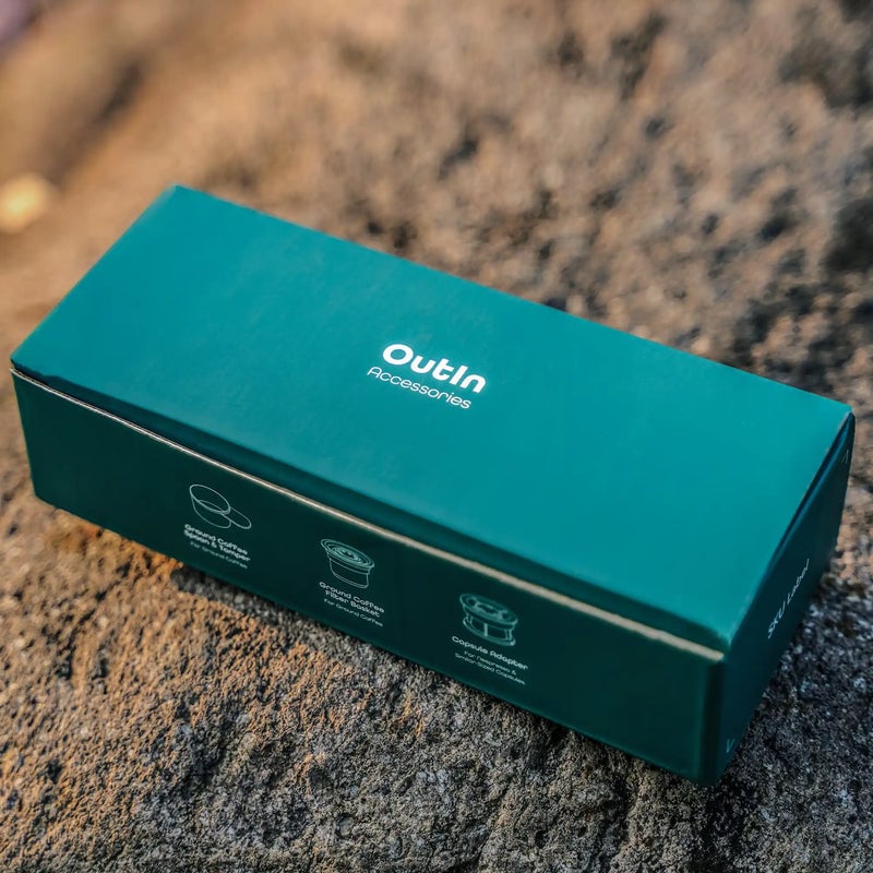 Зелена кутия „OutIn Accessories“ е на кафява повърхност близо до комплект адаптери Outin Nano. Зелена кутия „OutIn Accessories“ е на кафява повърхност близо до комплект адаптери Outin Nano.