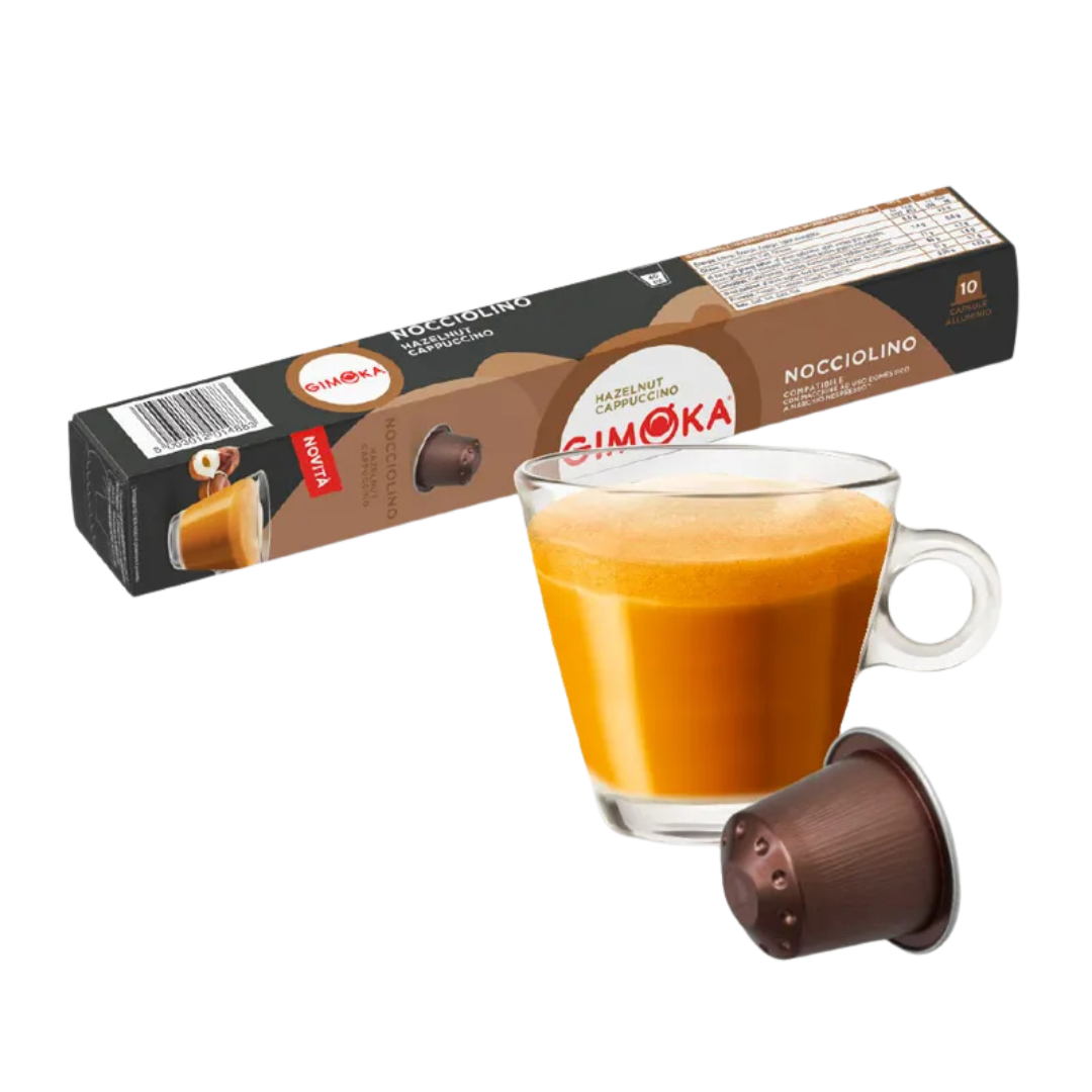 Outin капсула за кафе и чаша с пенлива напитка, разположени на фона на кутия Gimoka Pistacchino. Outin капсула за кафе и чаша с пенлива напитка, разположени на фона на кутия Gimoka Pistacchino.