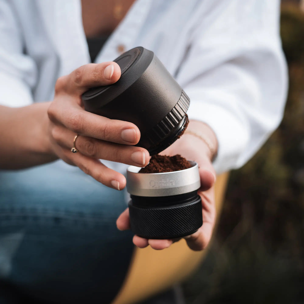 Лице, използващо кафемелачка Outin, изсипва прясна утайка в контейнер на открито. Лице, използващо кафемелачка Outin, изсипва прясна утайка в контейнер на открито.