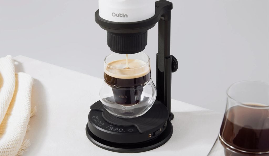 Кафемашина за еднократна употреба Outin, която дозира еспресо в чаша от прозрачно стъкло върху бял плот.