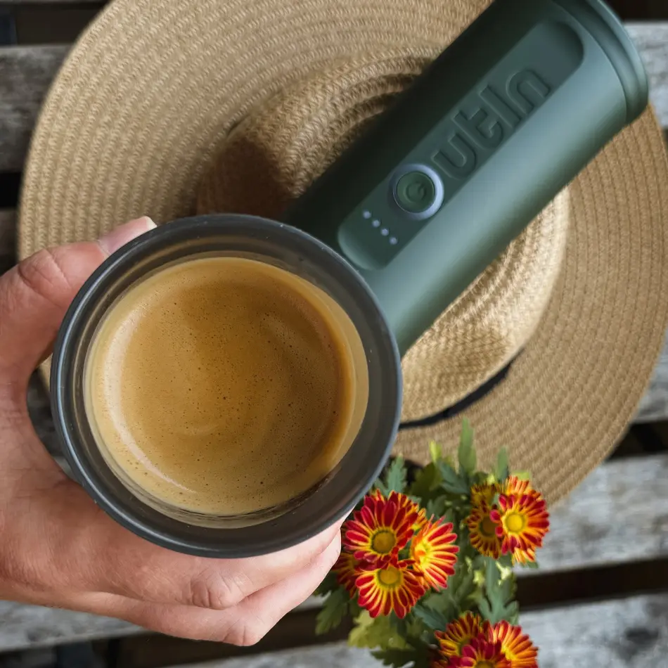 Ръката държи кафе над сламена шапка, със зелен термос - Перфектен подарък за любител на кафето - сред червено-жълти цветя.