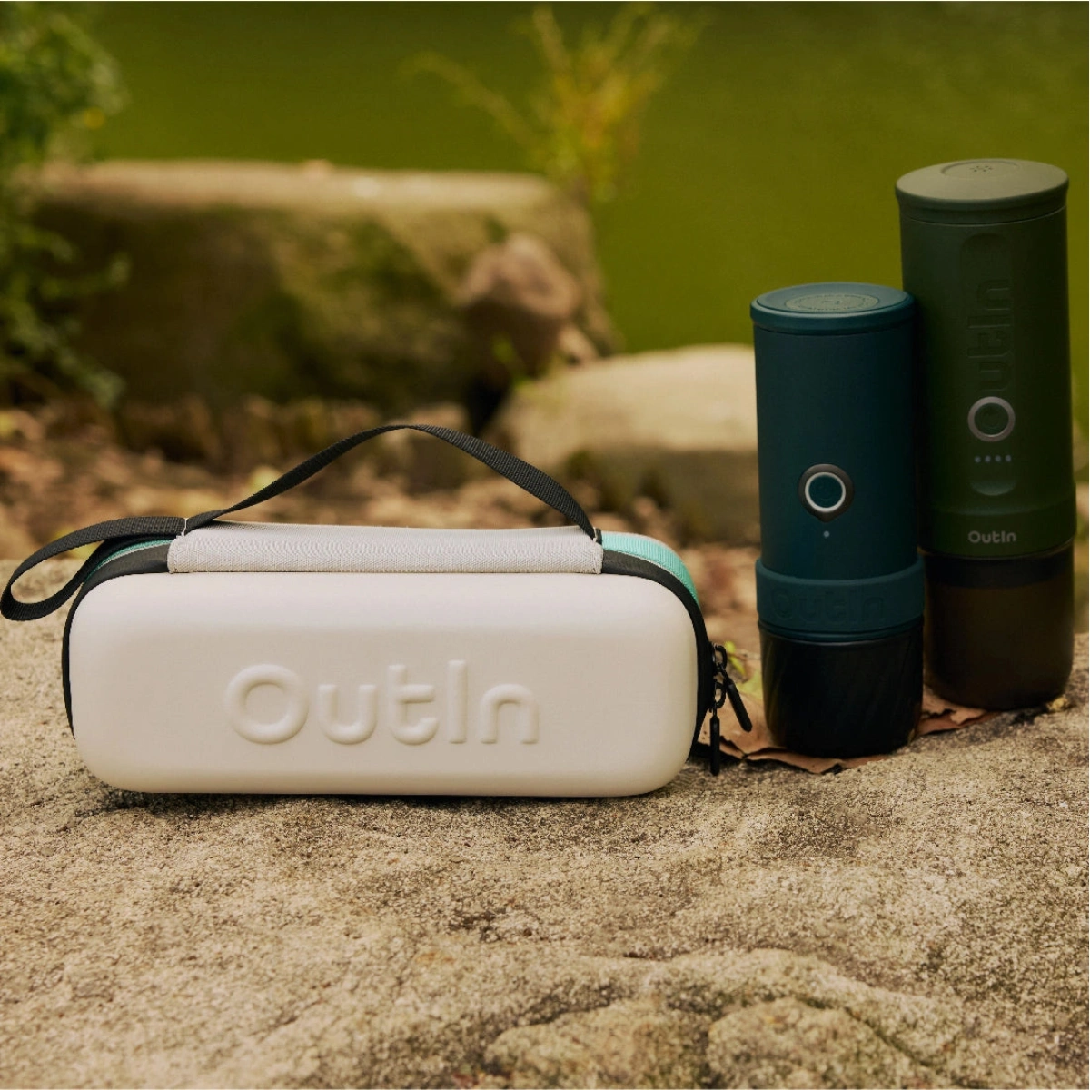 Бял куфар Outin и две зелени цилиндрични устройства лежат на скала близо до езеро. Бял куфар Outin и две зелени цилиндрични устройства лежат на скала близо до езеро.