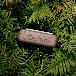 Кафяво устройство Outin с водни капки лежи върху буйни зелени папрати на открито.