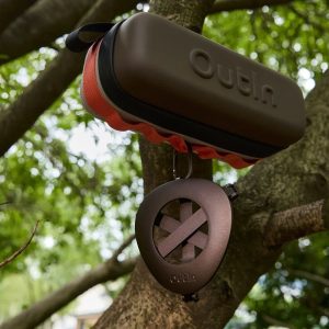 Калъф с твърда обвивка от Out-In и преносим уред за защита от насекоми висят на клон на дърво на открито.